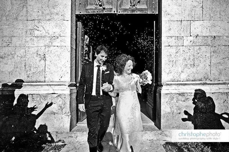 Black and white shot of the bride and broom walking out the Church. Shadows of people can be seen throwing rice to the newlywed couple. Shot by wedding photographer pisa venice italy christophe viseux 