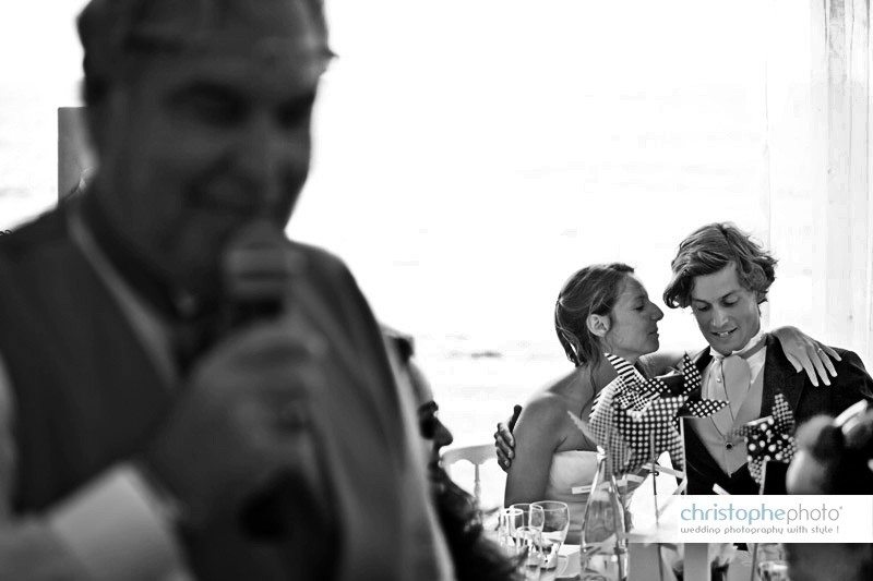 Candid moment between the newly wed couple while the father of the groom is giving a speach. Image taken by Wedding Photographer France