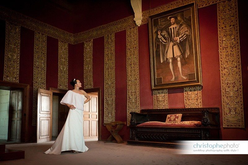 Bride posing in front of a portrait of French King François the first in Chateau de Chambord, France. Directed by wedding photographer france